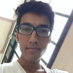 Rishi Lodha with short dark hair and glasses looks at the camera, standing indoors near large windows, wearing a white shirt.